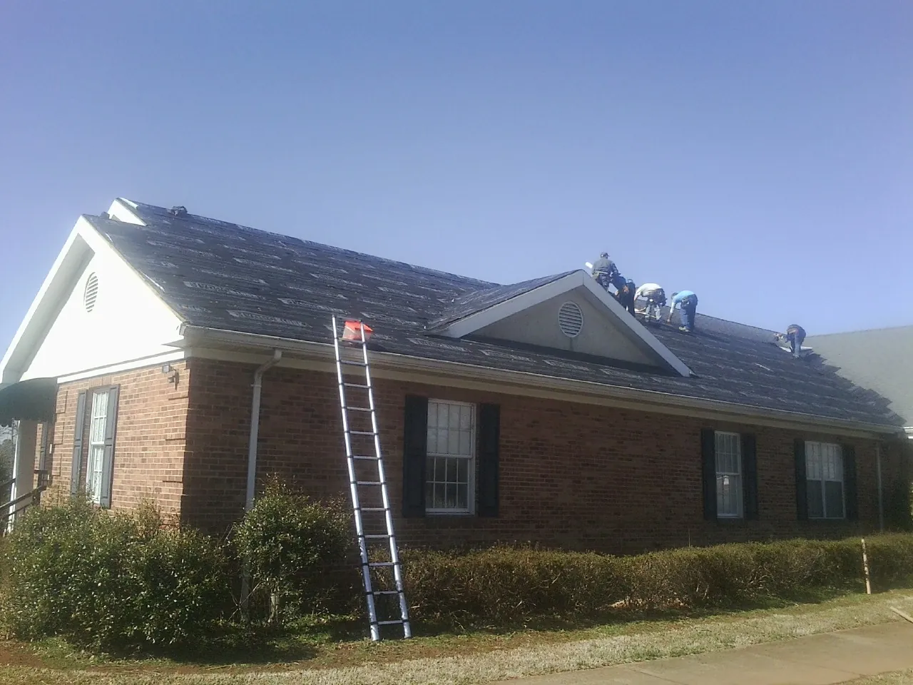 Crew tearing shingles off a brick ranch roof with a ladder set — Metal Roof Repair work by our crew in Hawthorne