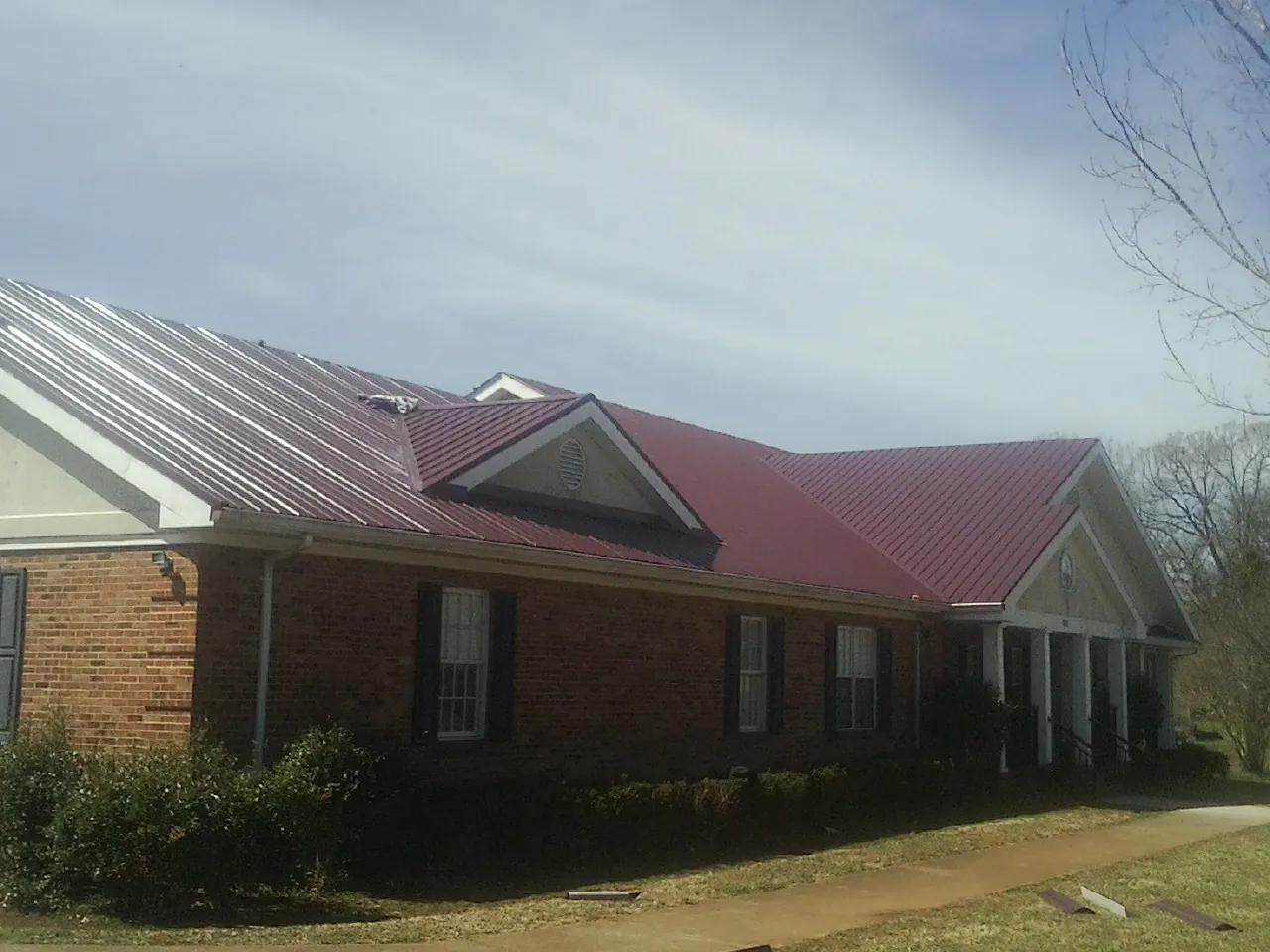 Red metal roof with gabled entries on a long brick building, from a Hail Damage Roof Repair job in Hawthorne