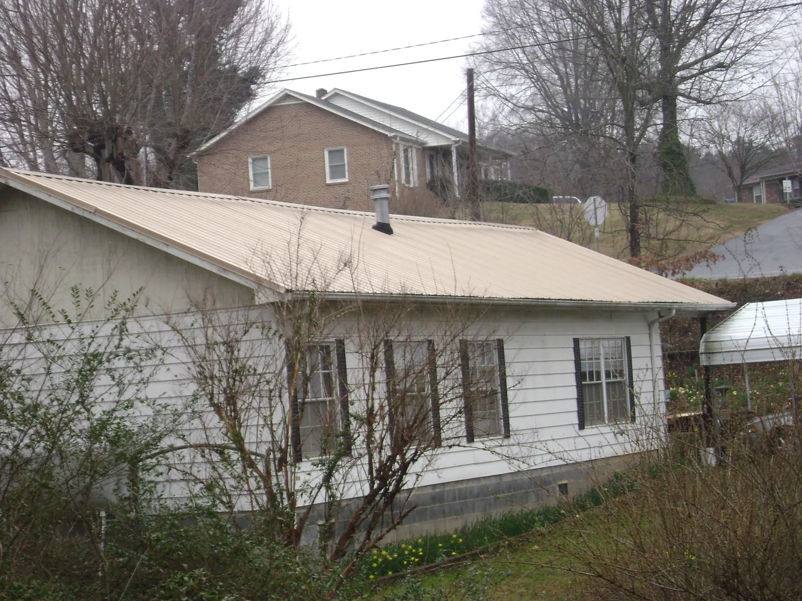 Tan metal roof on a white sided house set into a hillside — Commercial Roofing by Roofing Brothers in Hawthorne